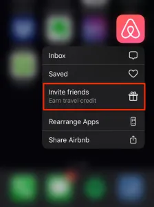 The screenshot shows the Airbnb mobile app icon with a blurred background of other apps and iPhone interface. Below the Airbnb icon, there is a section with a gift icon and text that says “Invite friends”.