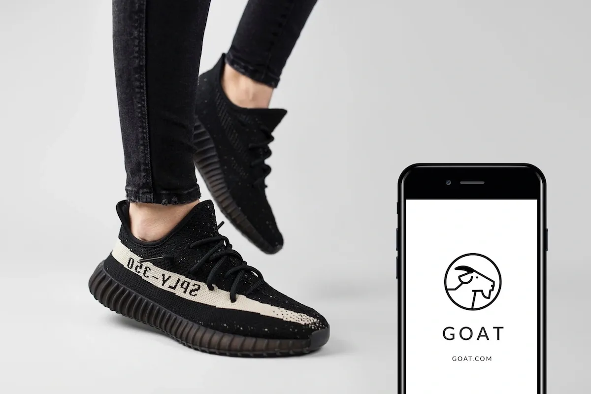 black sneakers with white stripes and a display of the GOAT app on a smartphone device